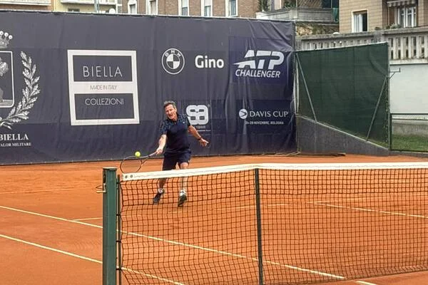 Un joueur du CCN en revers sur la terre battue de Biella, bannières ATP Challenger en fond